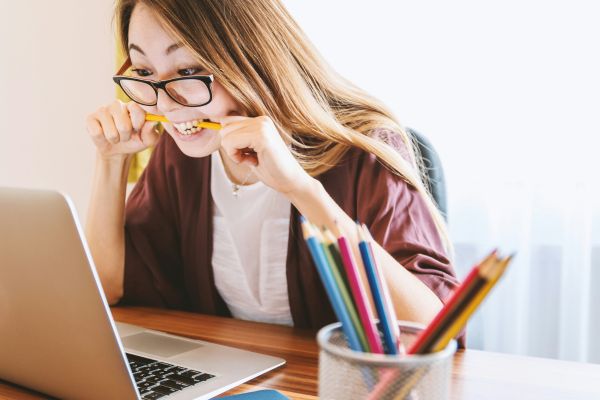 Professional woman in a home office focusing intensely on her laptop while biting a pencil